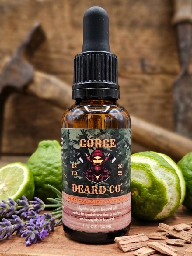 A 1 fl oz amber glass dropper bottle of Beard Co. Beardroom Wood Gorge Beardboard Oil, styled on a rustic wooden surface with limes, lavender, and wood chips.